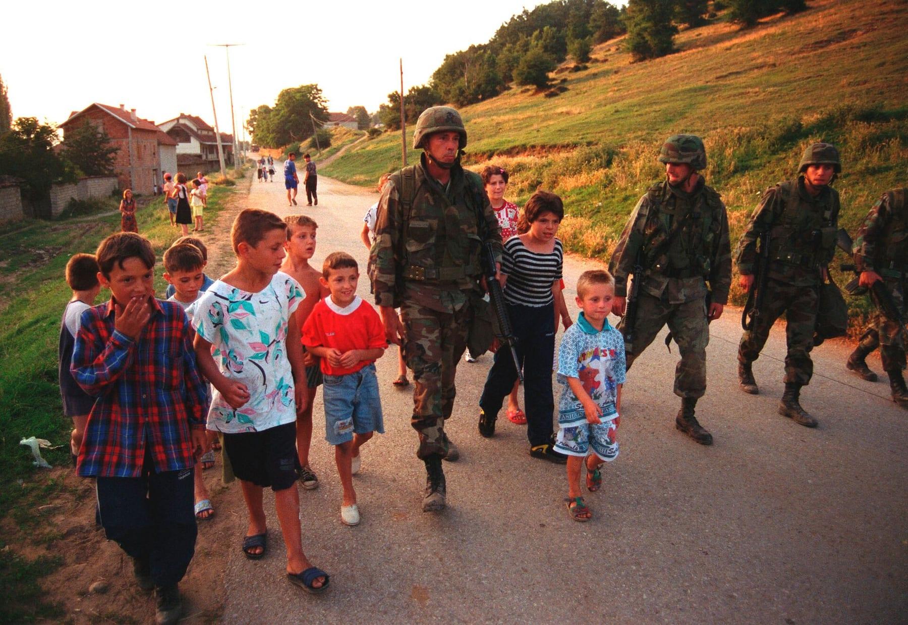 Soldiers and a group of children walk together along a village road.