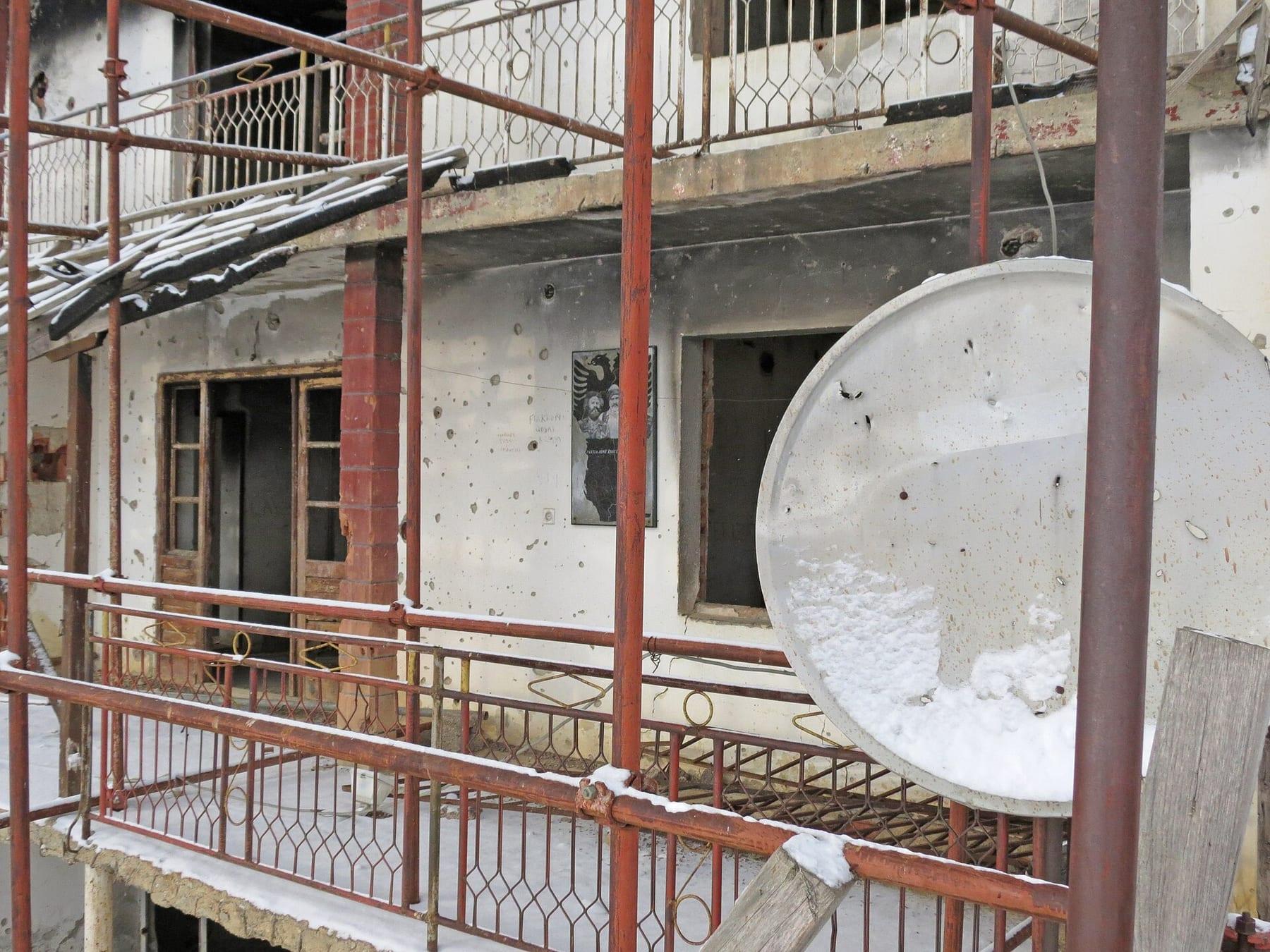 House façade pocked with bullet holes, surrounded by protective metal scaffolding.