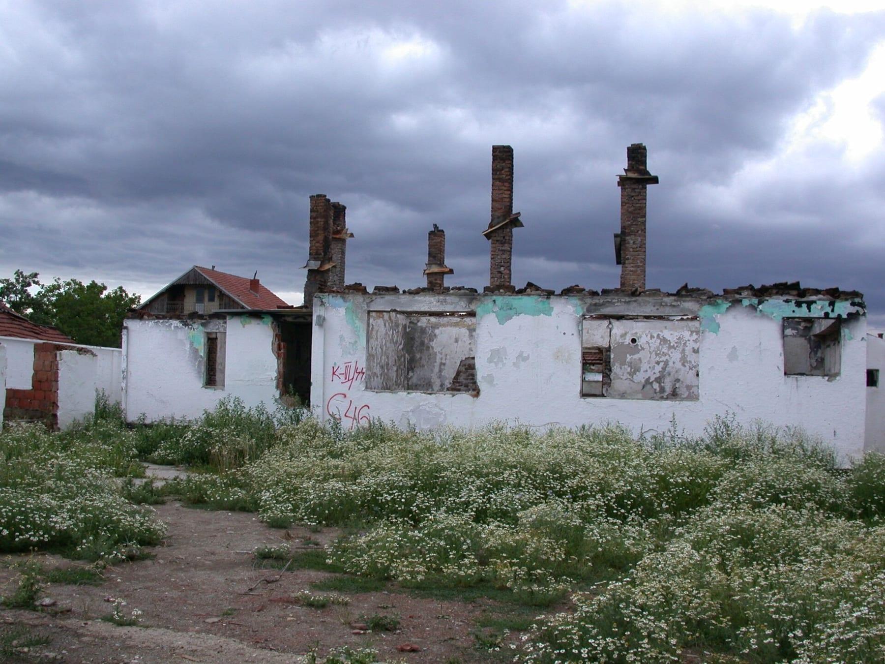 Roofless white-walled house with only chimneys standing, under a cloudy sky.