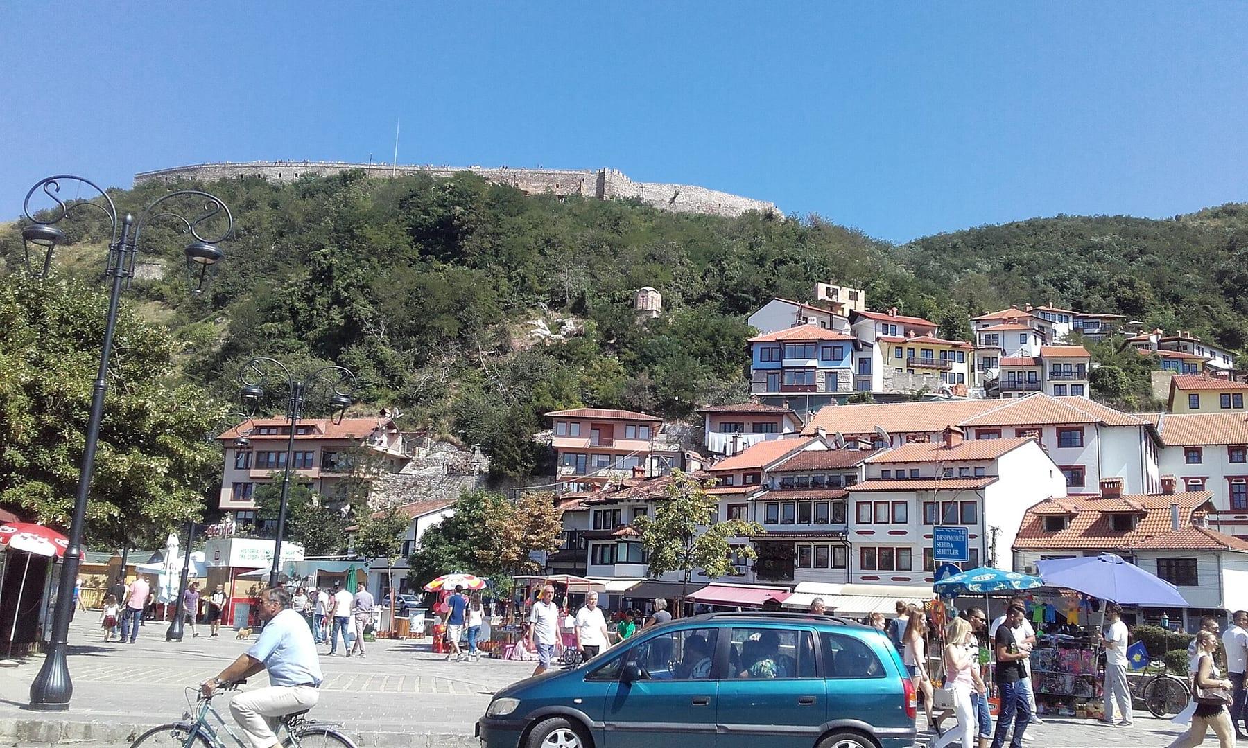 Traditional houses on the slope, the fortress on the hilltop and people in the square.