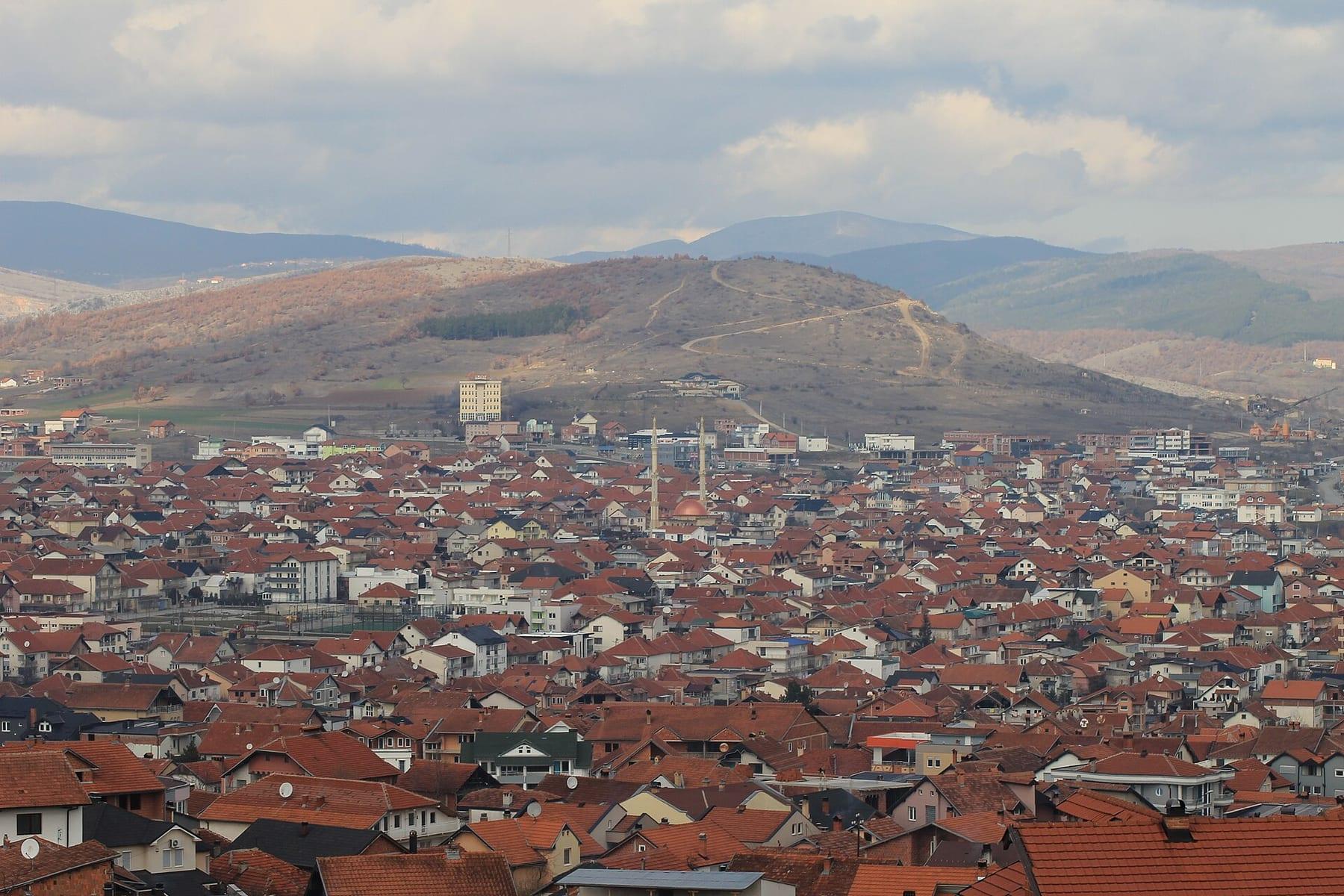 Wide view of the red-roofed city with hills behind.