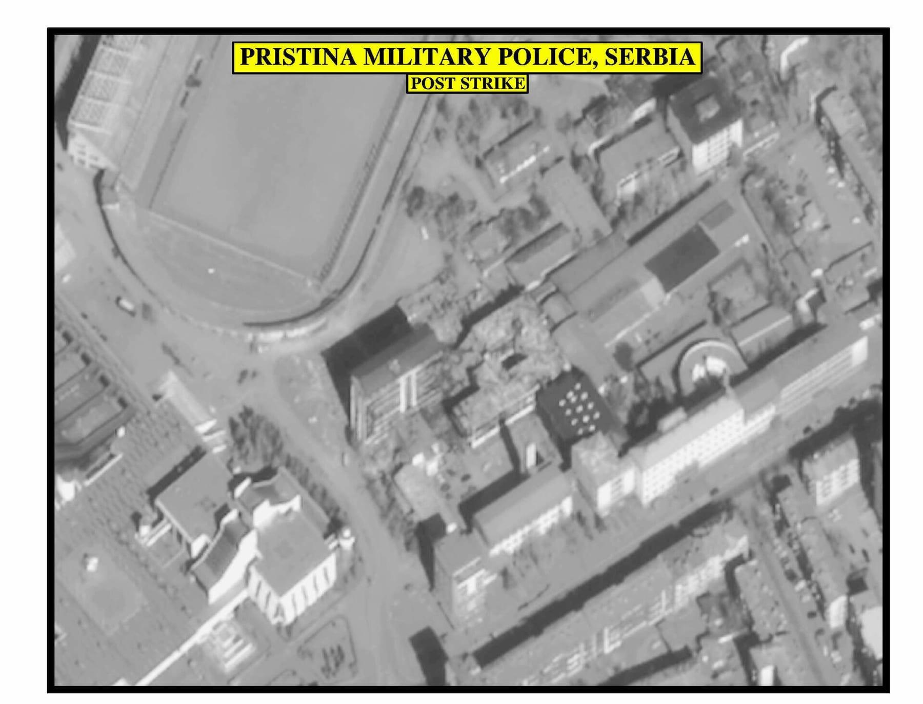 Black-and-white aerial image of a city district with a stadium and damaged buildings.