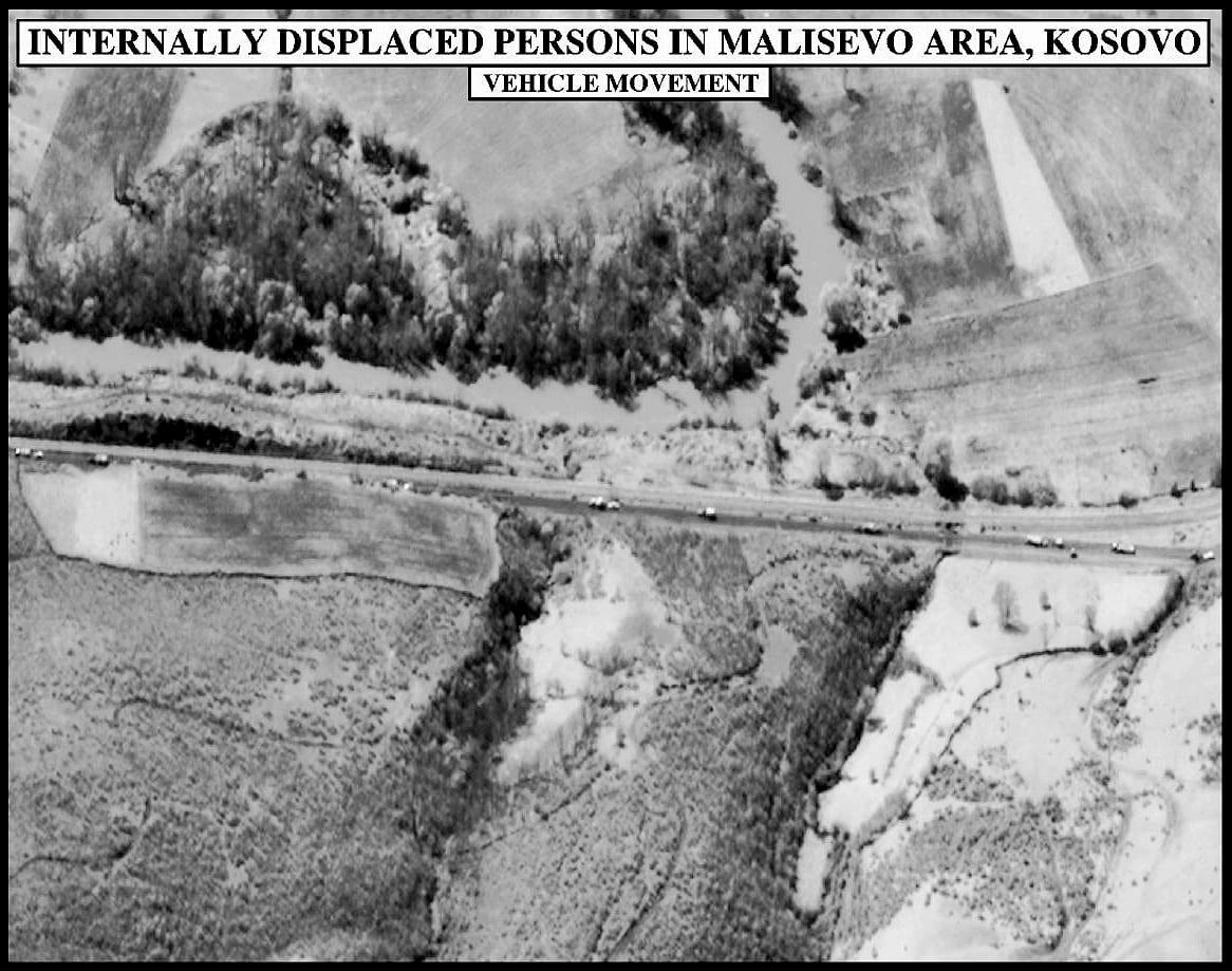 Black-and-white annotated aerial photo showing a column of vehicles on a road between fields.