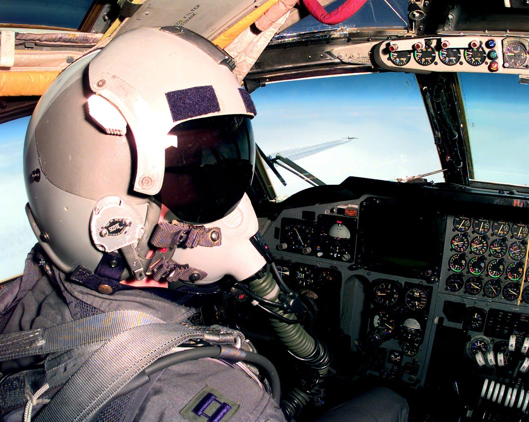 A helmeted, masked pilot in a bomber cockpit with the instrument panel ahead.