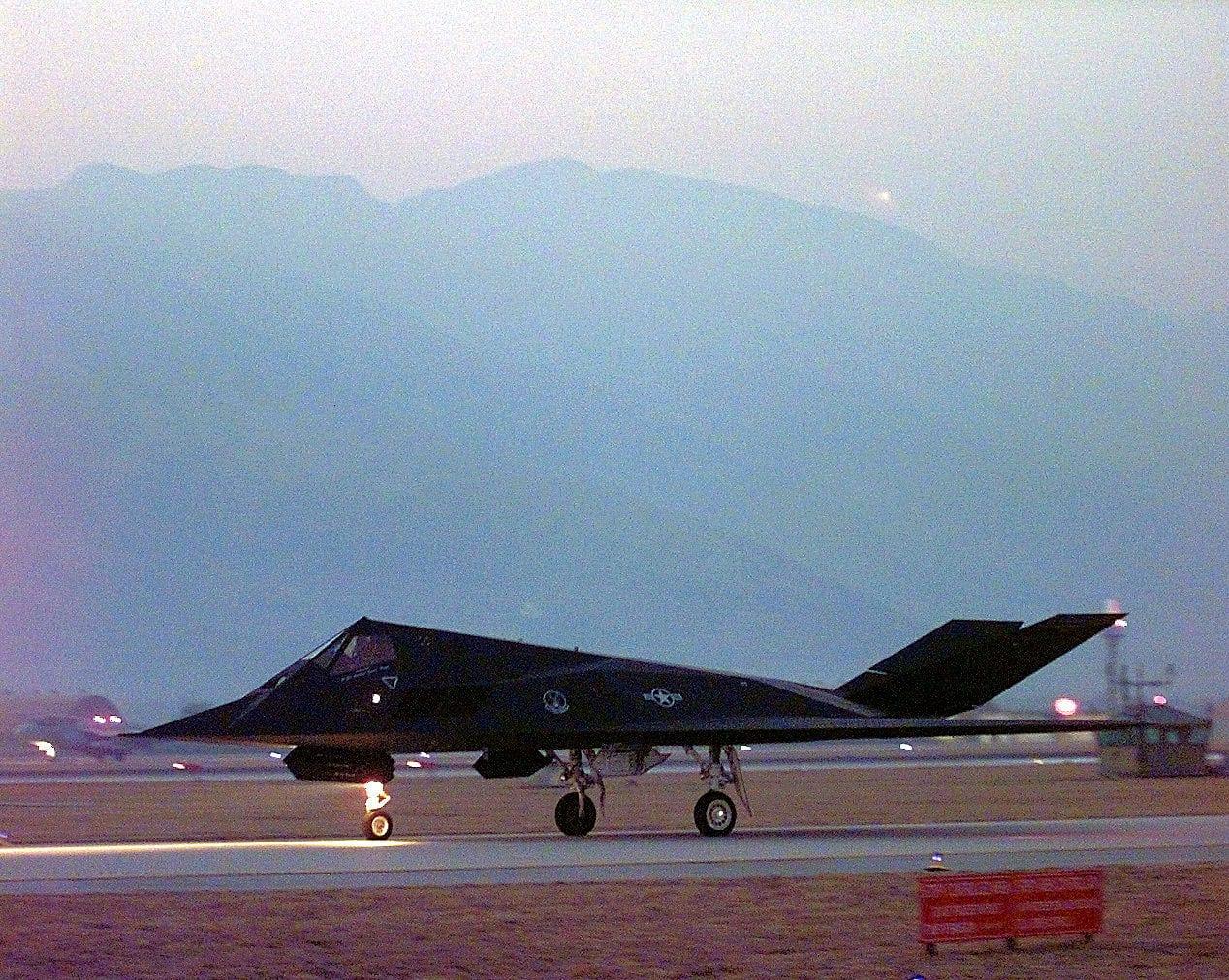 Black angular aircraft on the runway at dusk, mountains in the background.