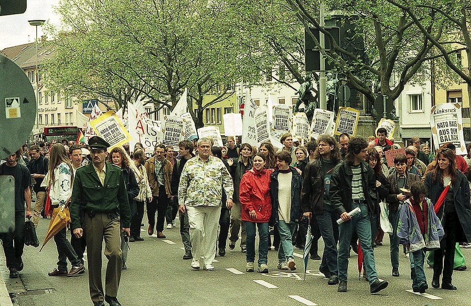 A column of demonstrators with placards walks down a city street.