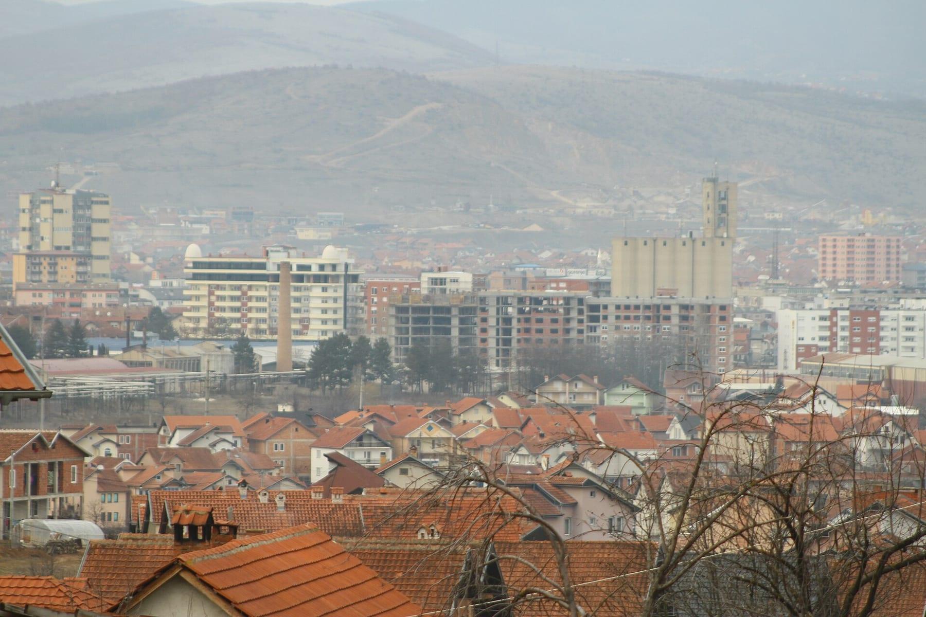 Central high-rises above red roofs, with haze and hills behind.