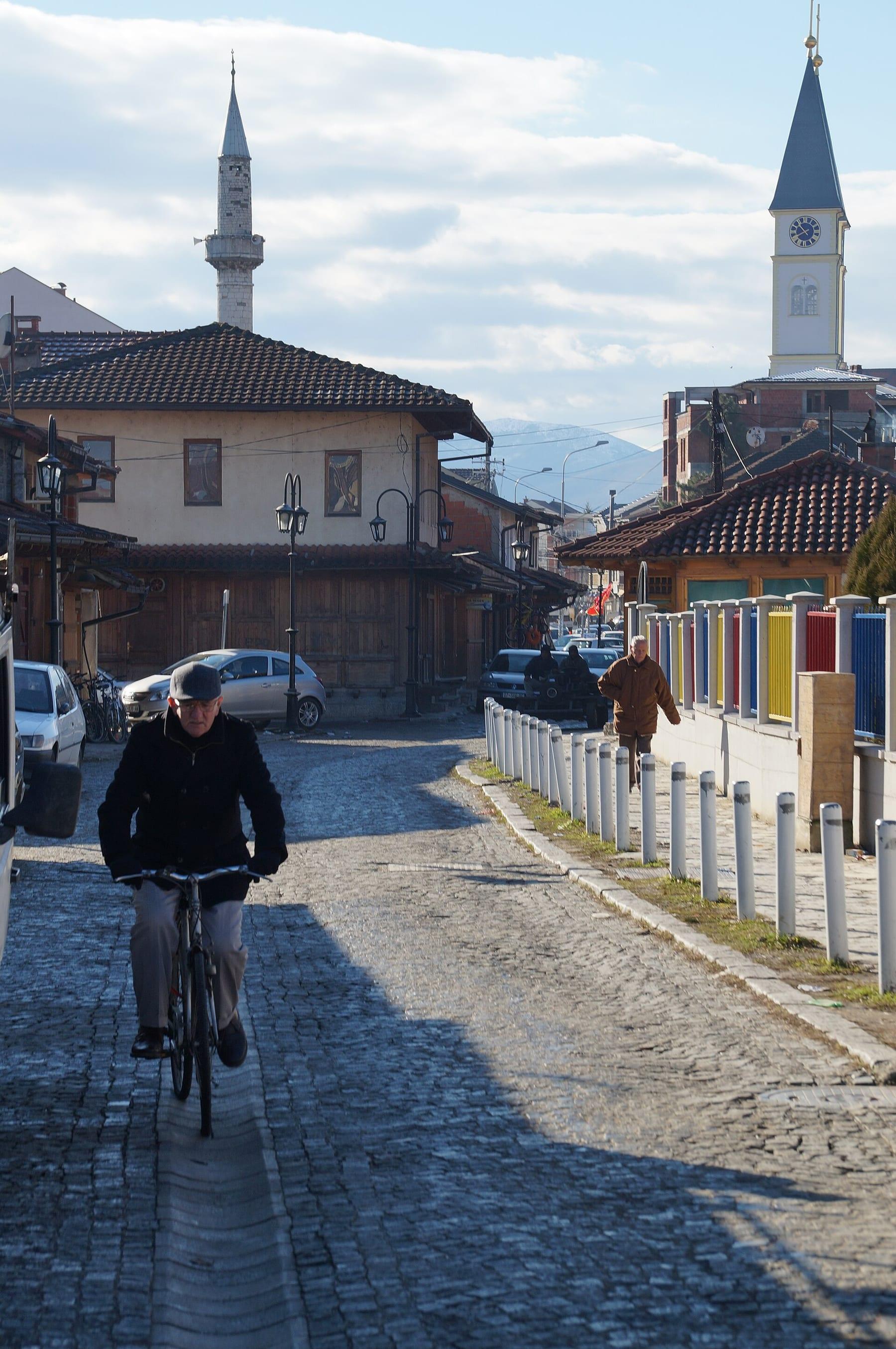 Cobbled street with a cyclist, traditional houses, a minaret and the clock tower.