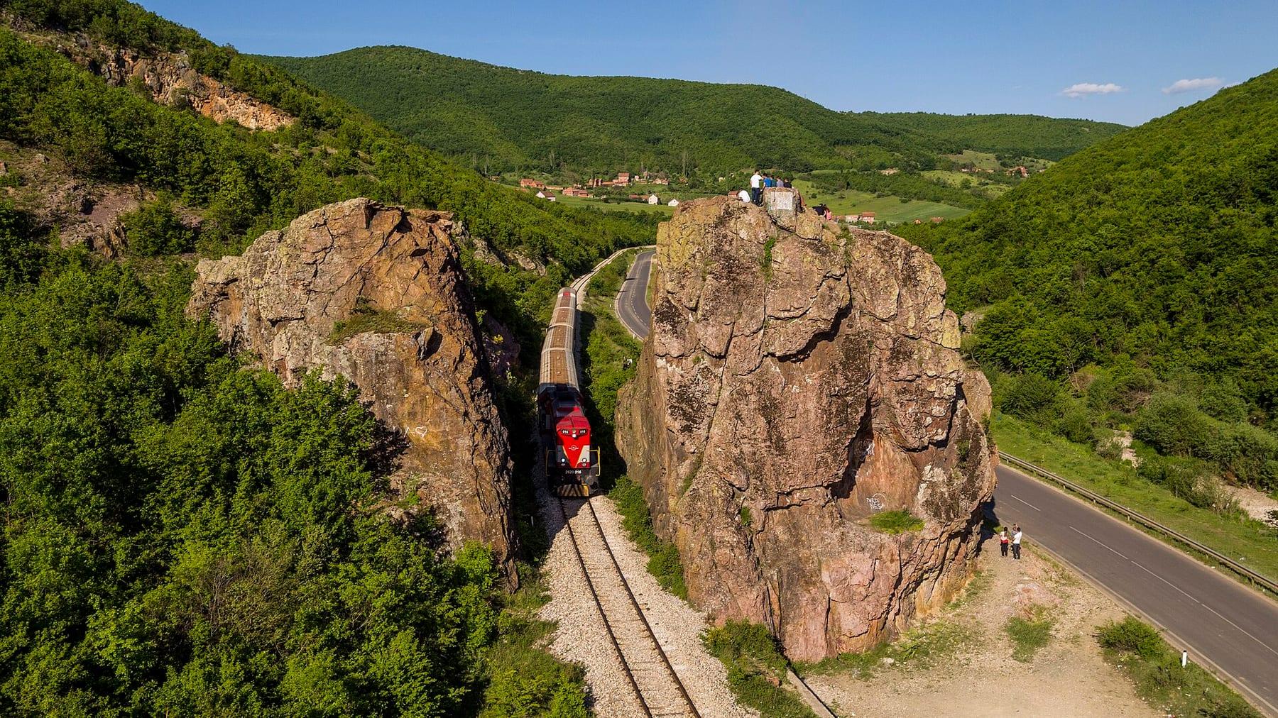 Two large rocks among green hills with the railway and a train passing between them.