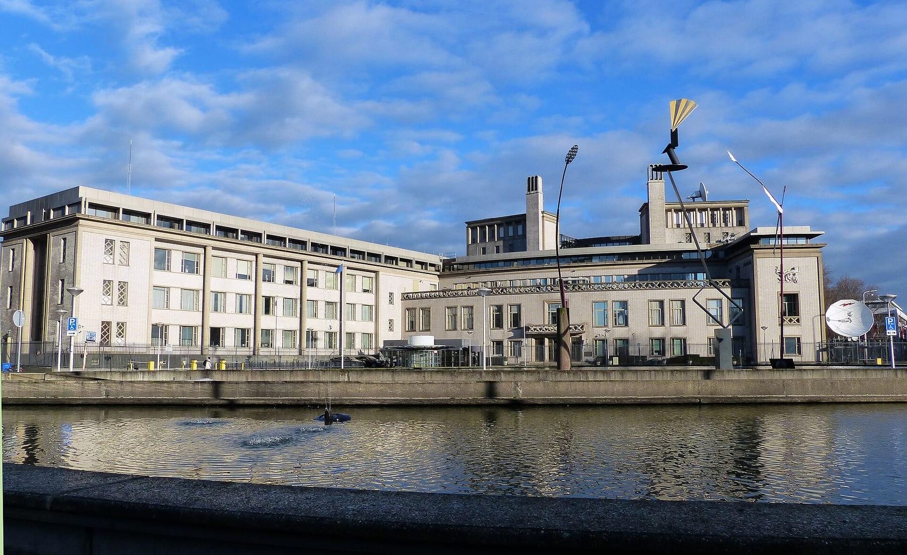 White court building with a pond in front, under a cloudy sky.