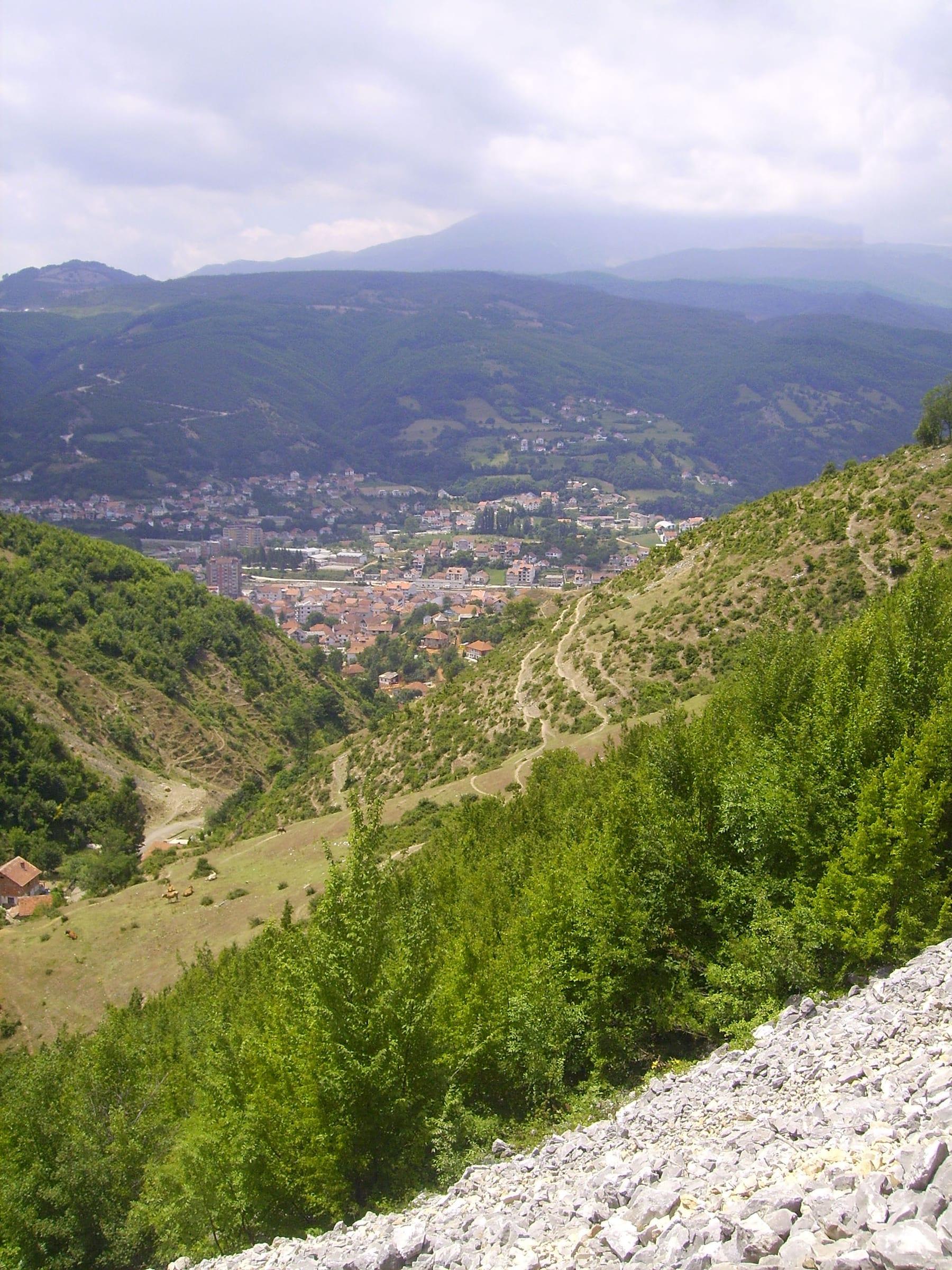 The town in a valley between green hills with mountains behind.