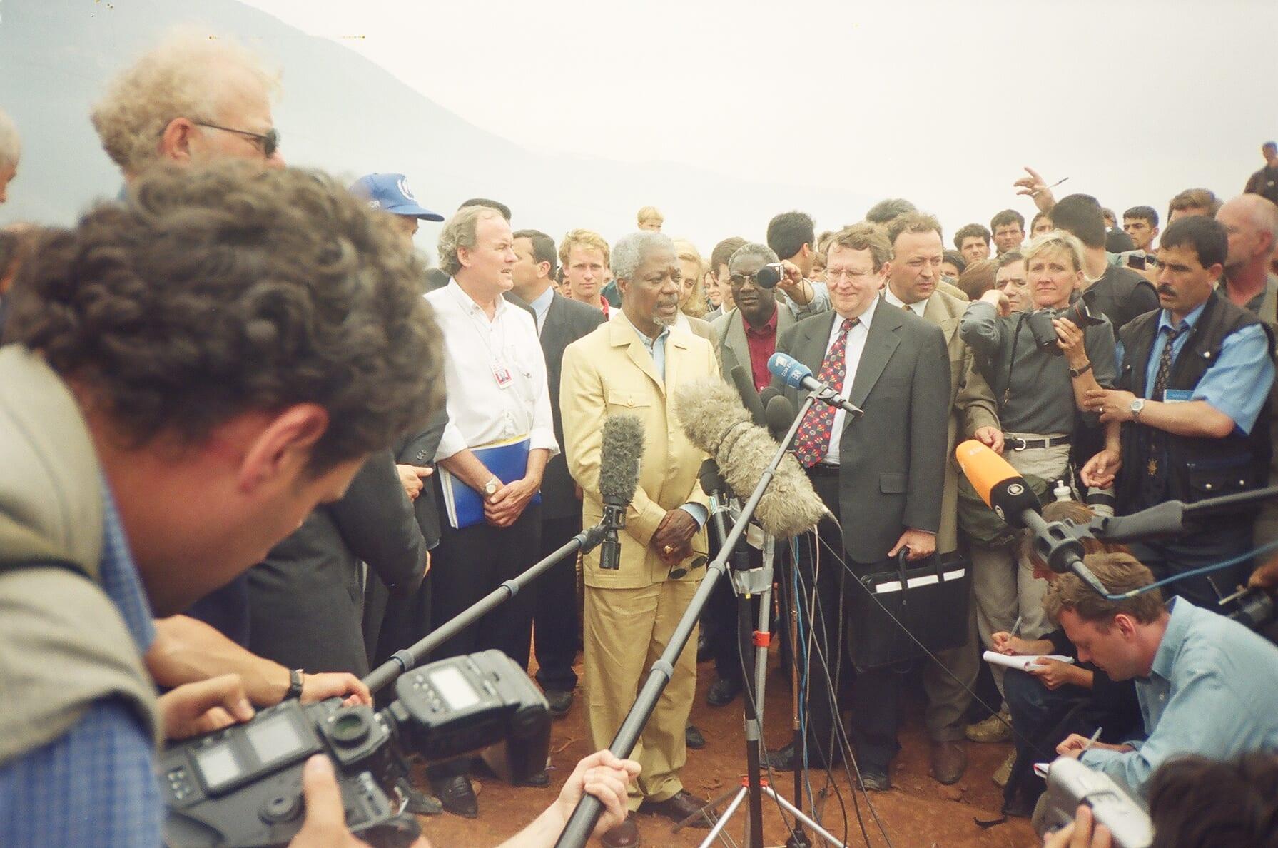 Kofi Annan at microphones, surrounded by journalists, camera operators and officials.