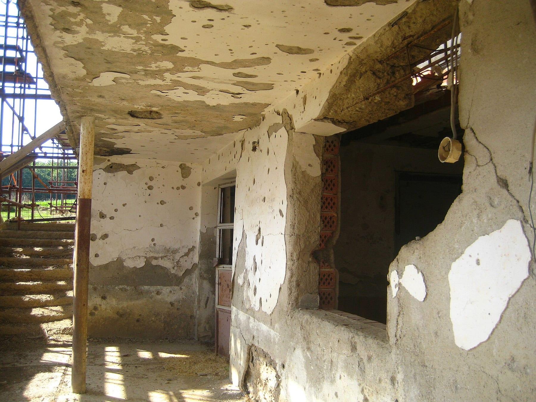House walls riddled with bullet and shell holes, with stairs and scaffolding.