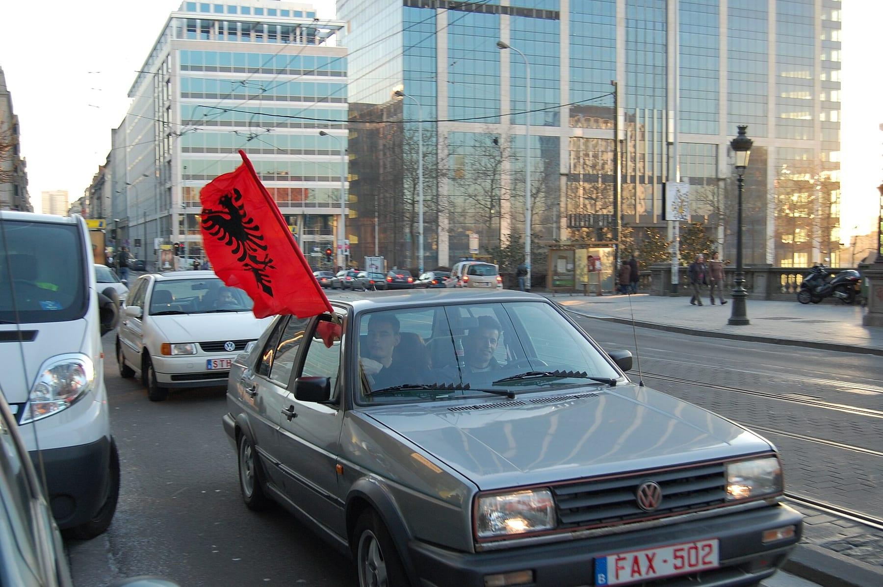 Cars on a boulevard with an Albanian flag flying from a window.