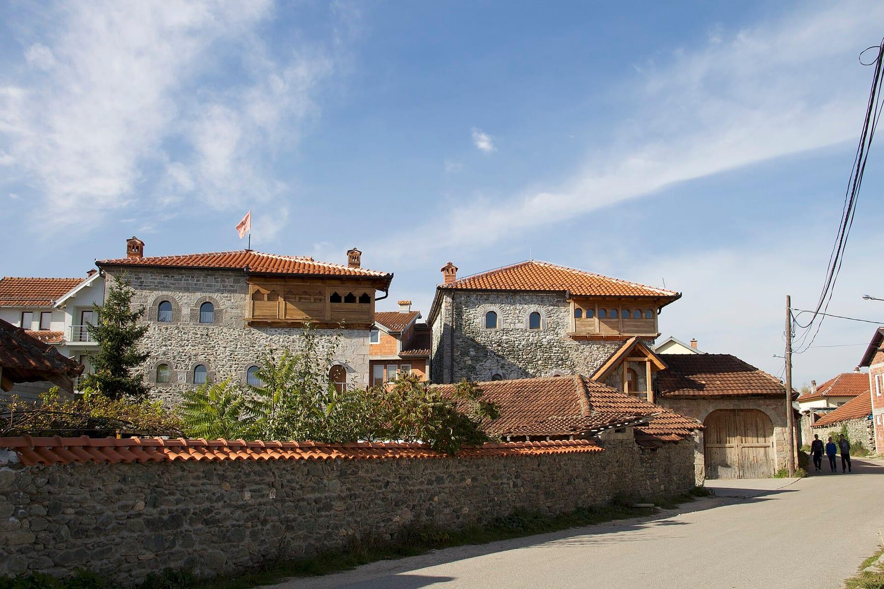 Traditional stone tower houses with red roofs beside a street in Junik.