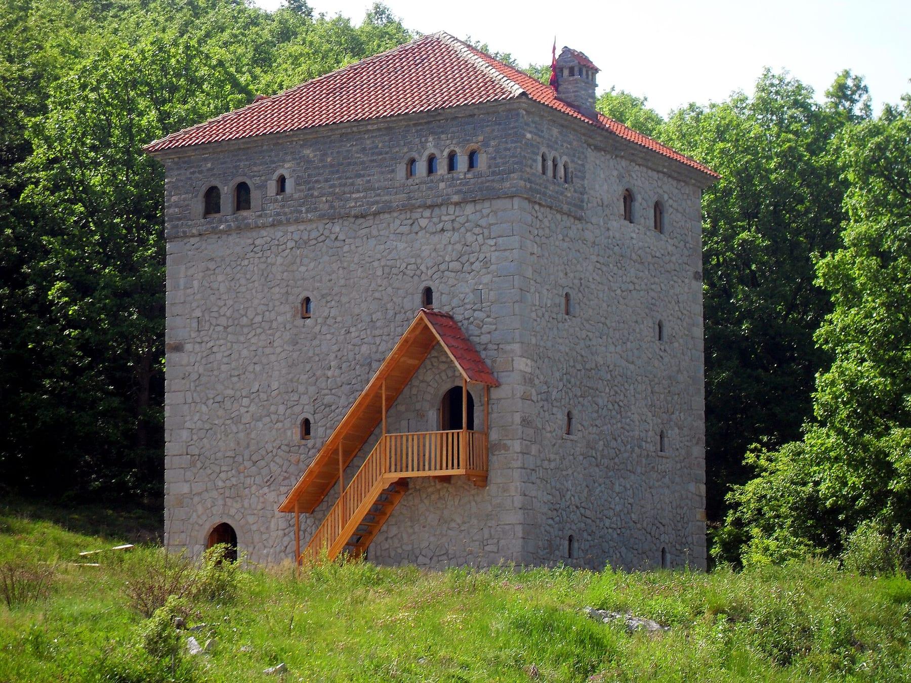 Stone tower house with red roof and external wooden staircase.