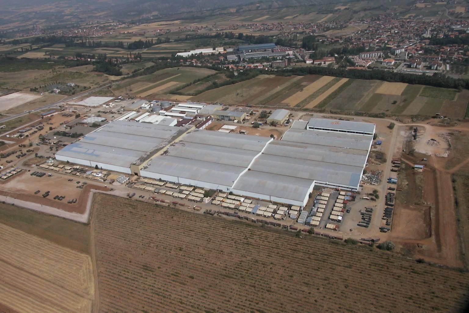 Large hall complex with containers and military vehicles, the town and fields around.
