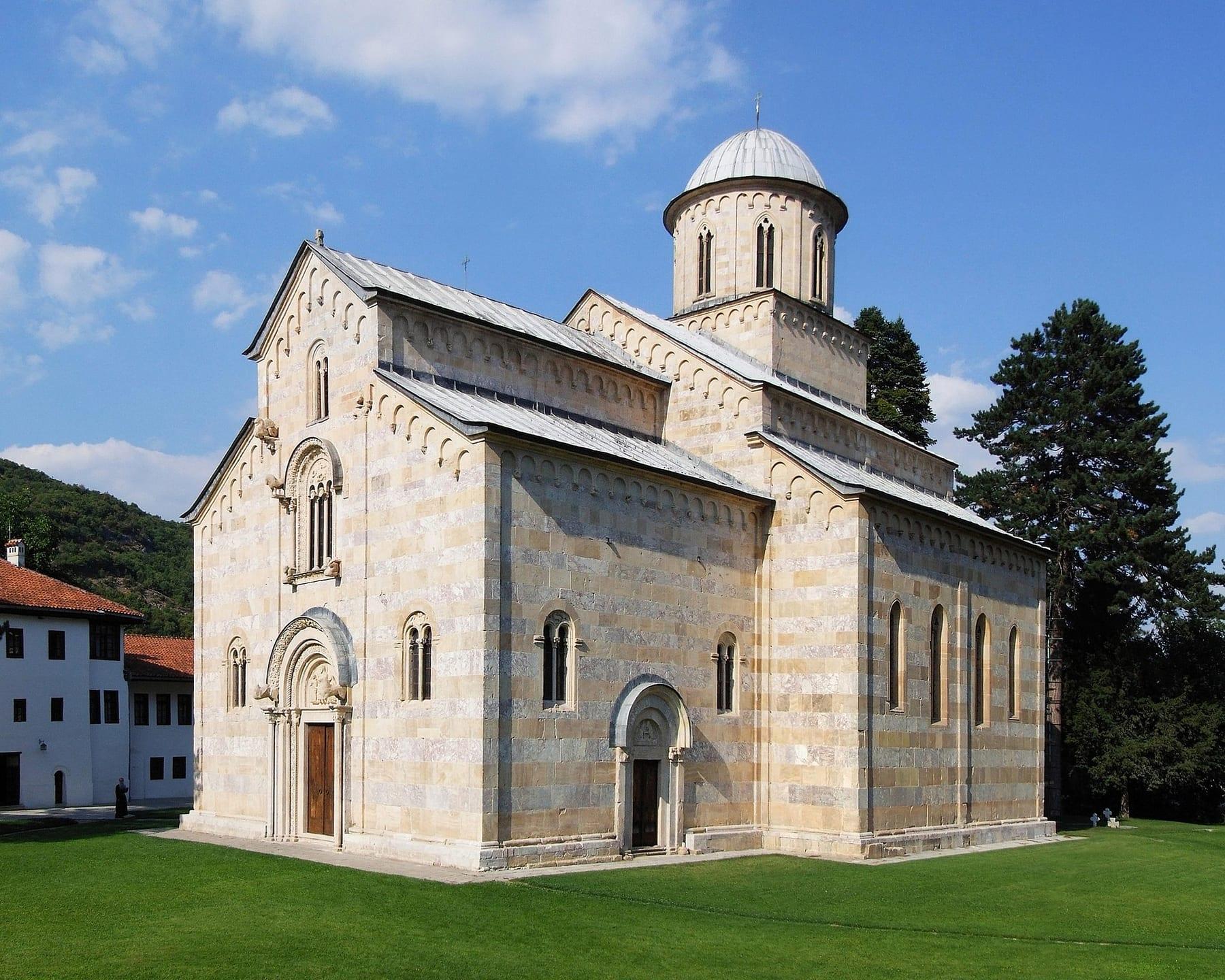 Medieval pale-marble church with a dome in a grassy courtyard.