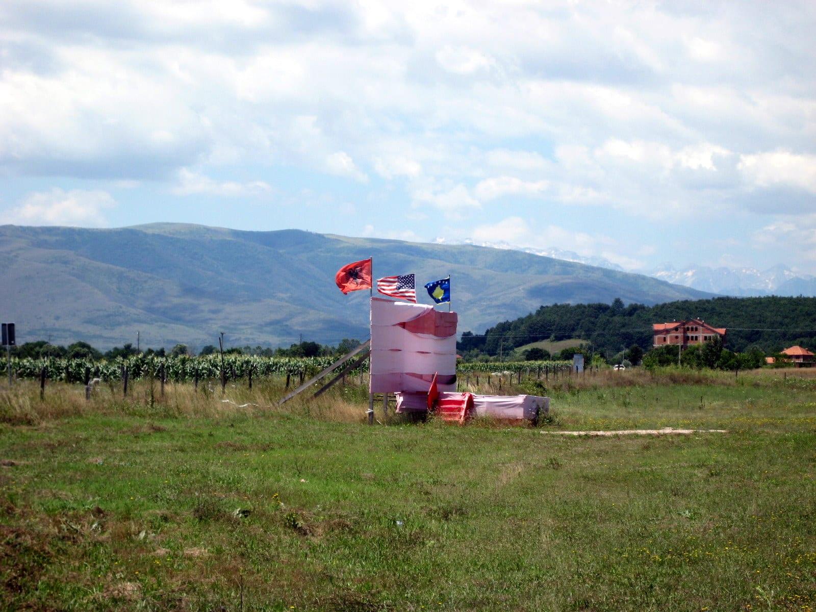 A green field with a memorial marker and flags, mountains in the background