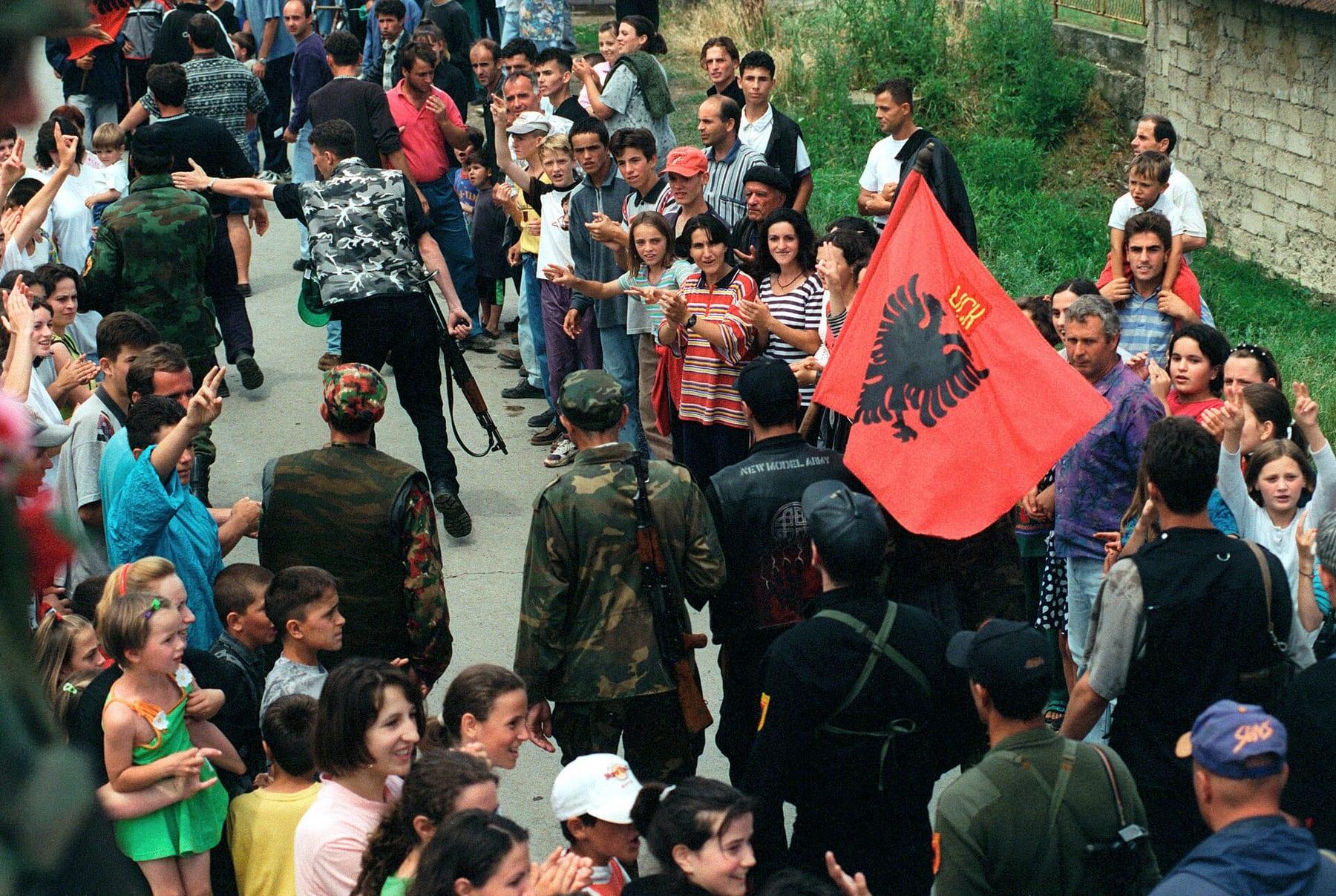 Uniformed men with an Albanian flag pass through a crowd of applauding residents.