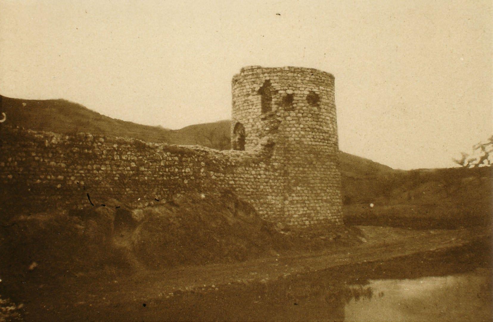 Sepia photograph of a round stone tower and fortress walls.
