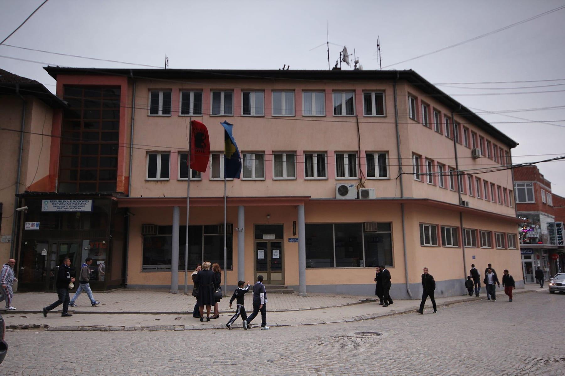 Three-storey administrative building with flags on a square with pedestrians.