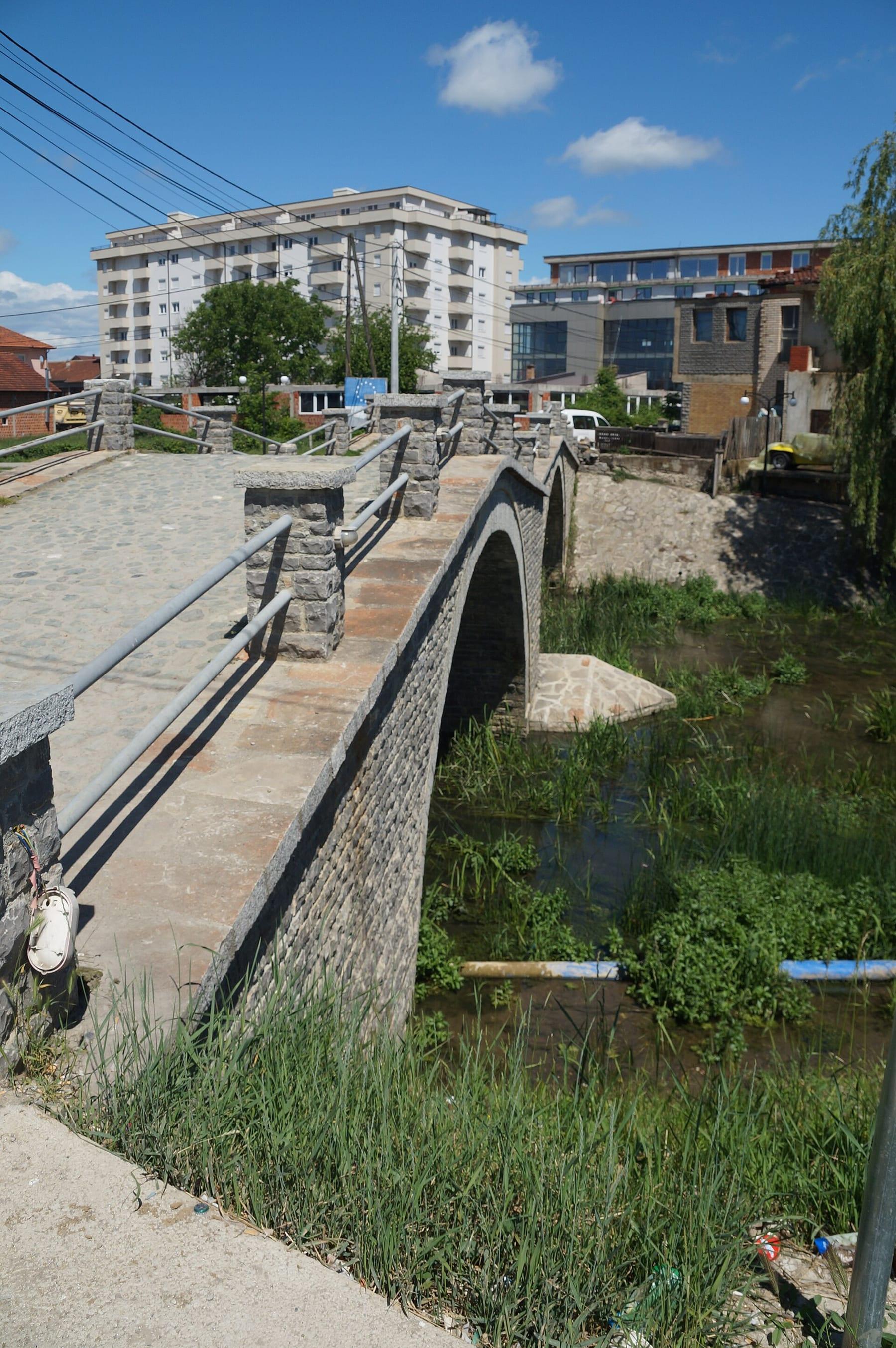 Old stone bridge over the river with town buildings behind.