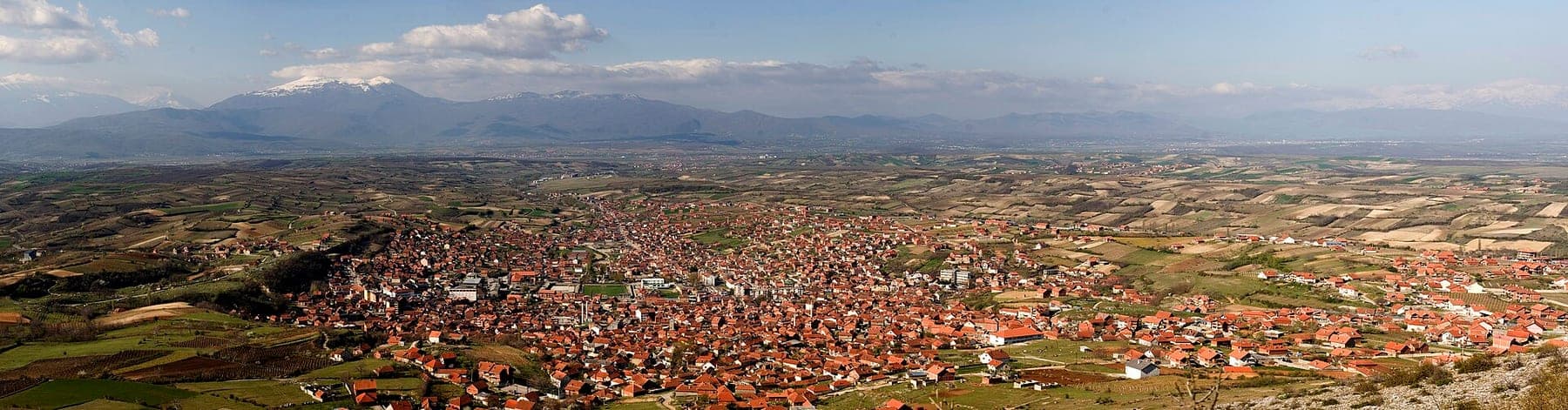Wide panorama of the red-roofed town on the plain with mountains on the horizon.