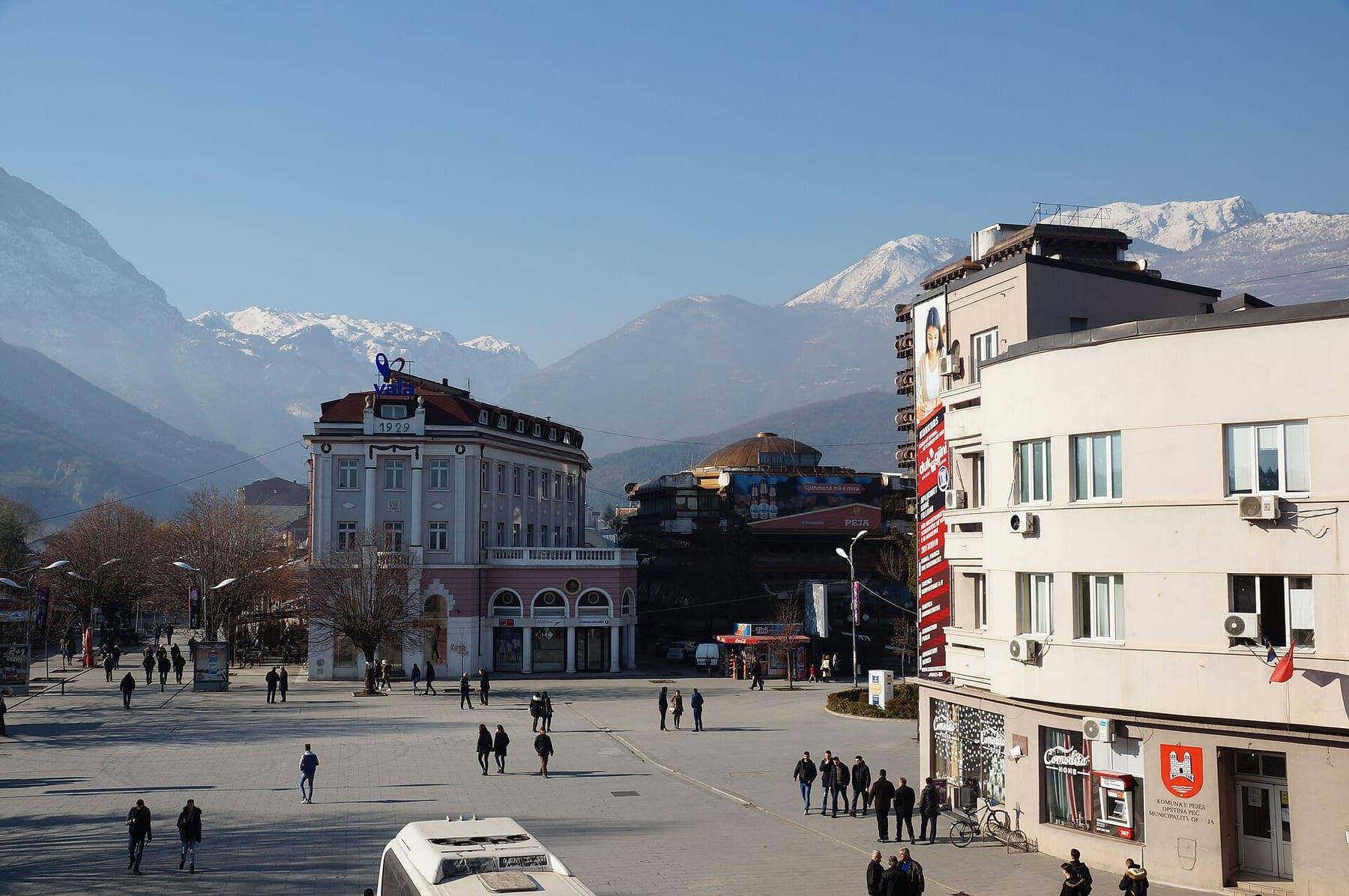 Central square with buildings and snow-covered mountains behind.