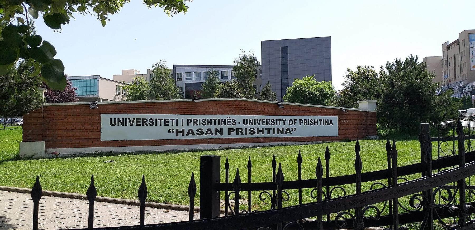 Wall bearing the university’s name, lawn and campus buildings behind.
