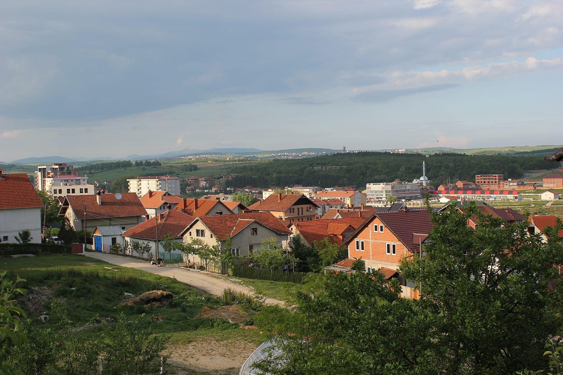 Red-roofed houses among greenery with hills on the horizon.