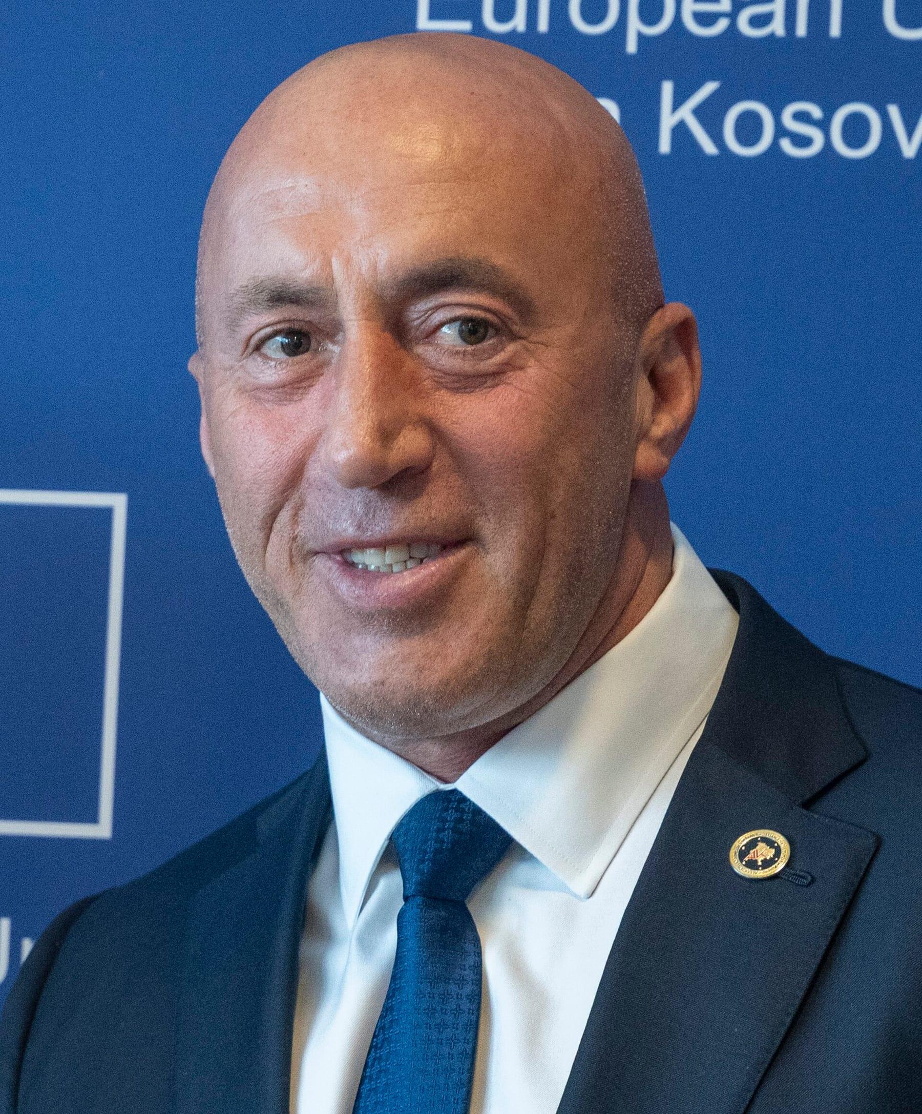Portrait of a smiling man in a blue suit and tie in front of a blue EU backdrop.