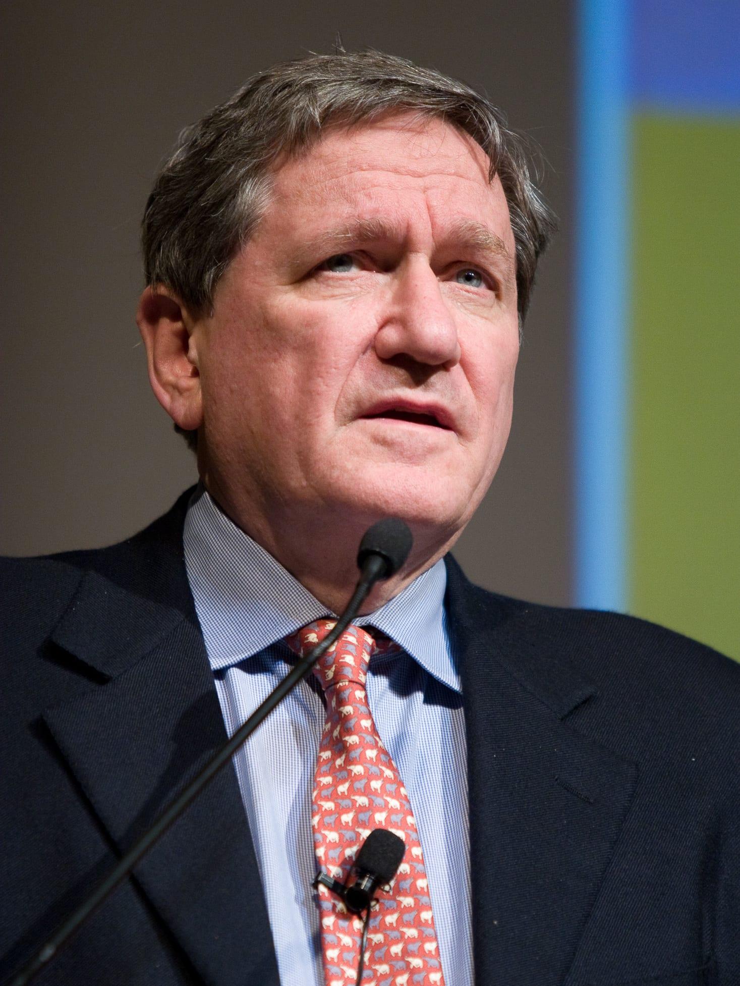 Man in a dark suit and dotted tie speaking at a microphone.