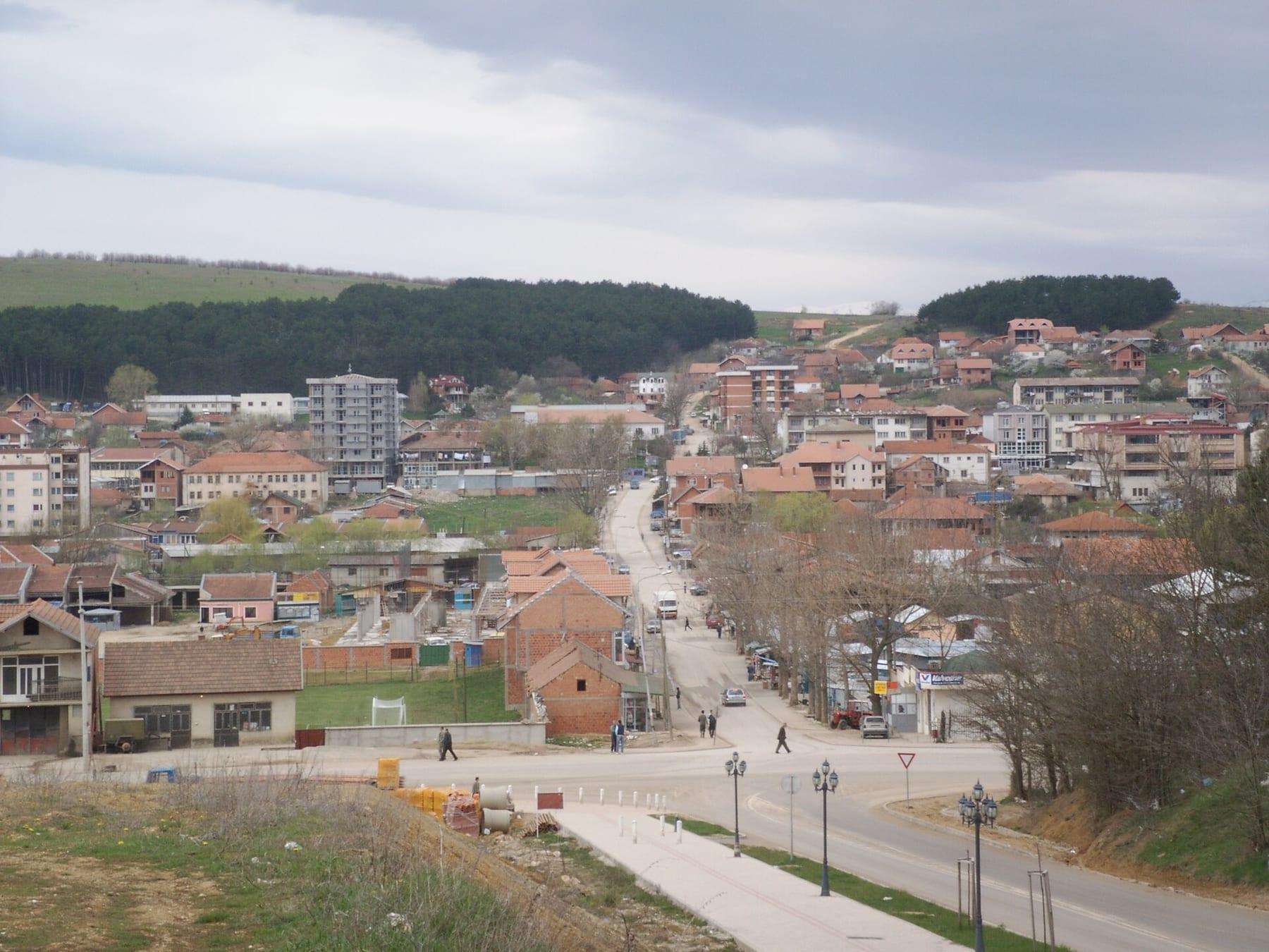Main road entering the town with houses and wooded hills.