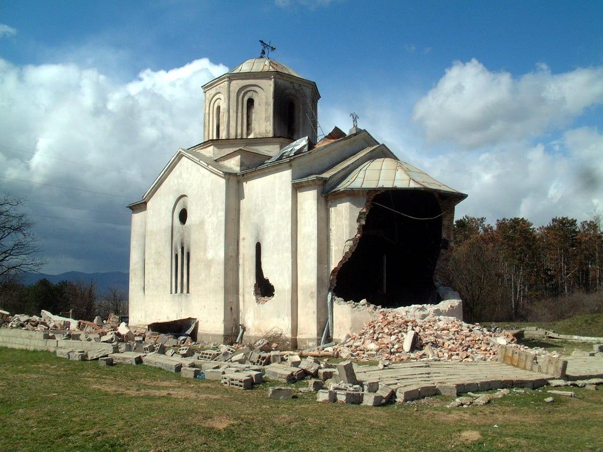 White church with a collapsed wall and rubble scattered around it.