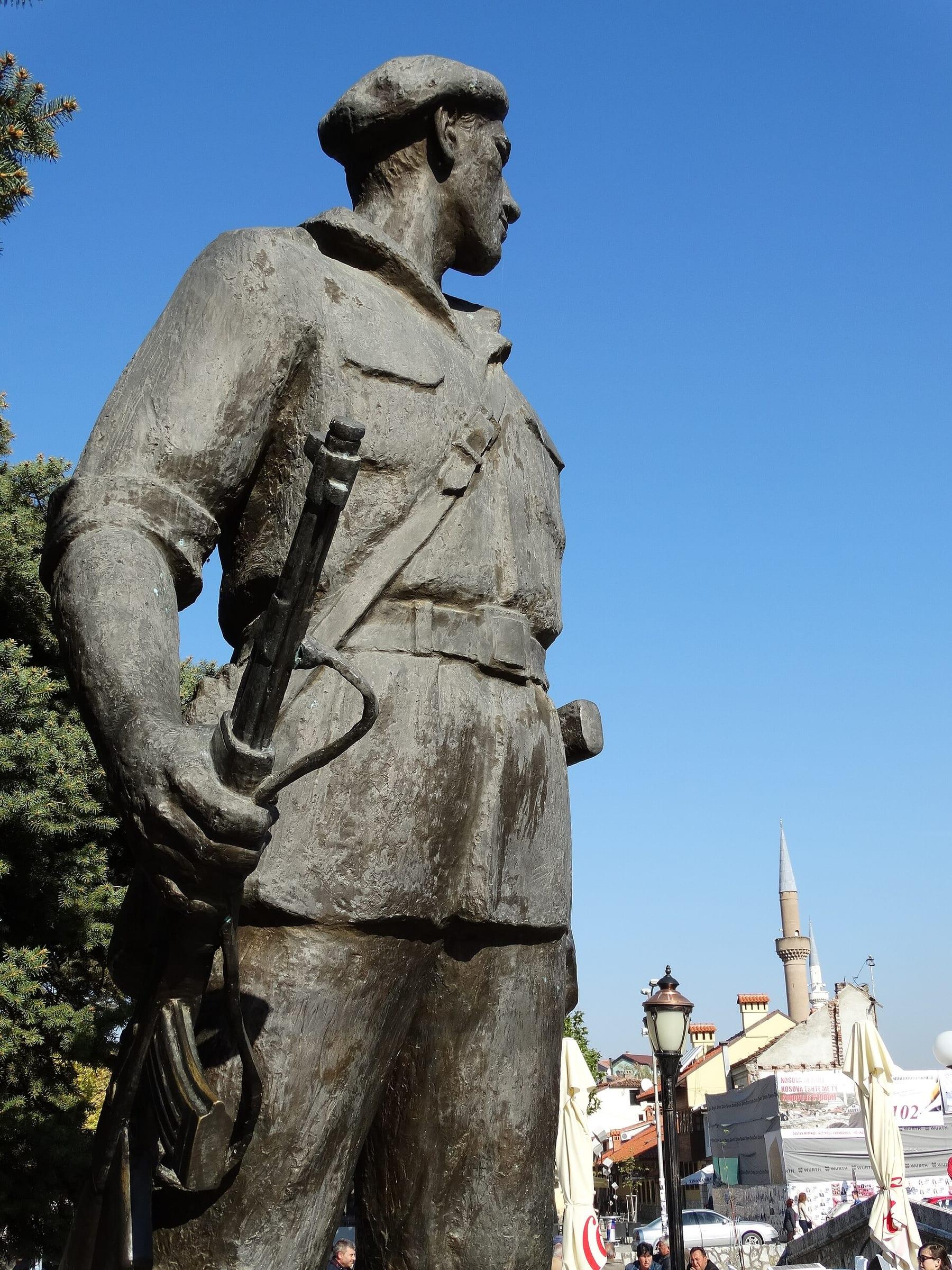 Bronze statue of a fighter in a beret against a blue sky; a minaret behind.