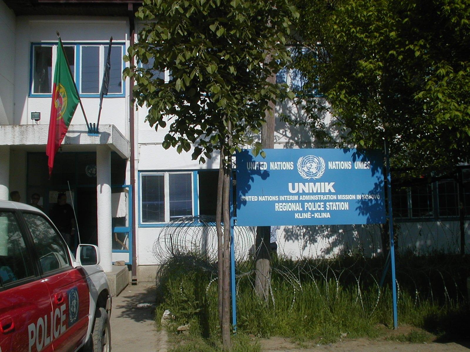 Building with a Portuguese flag and a blue UNMIK sign; a police car in front.