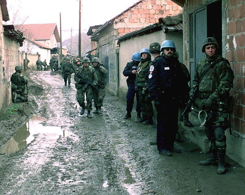 Soldiers and blue-bereted police in a muddy alley between houses.