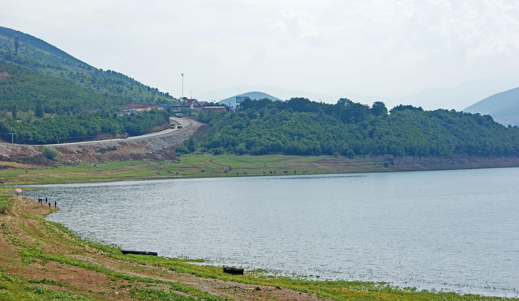 Lake with green shores and the border road on the slope beyond.