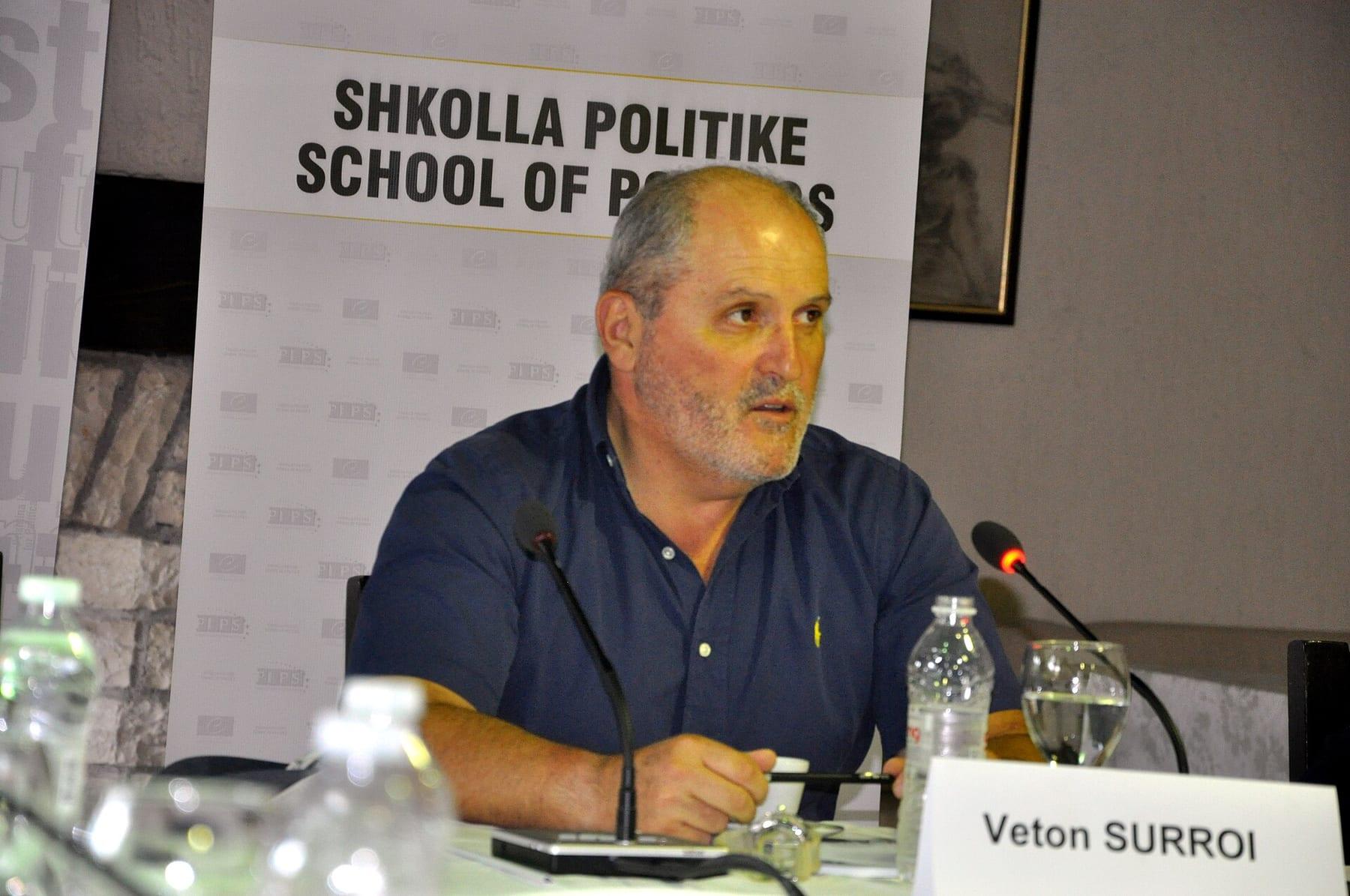 Man in a blue shirt seated at a table with a microphone and a name card reading “Veton Surroi”.