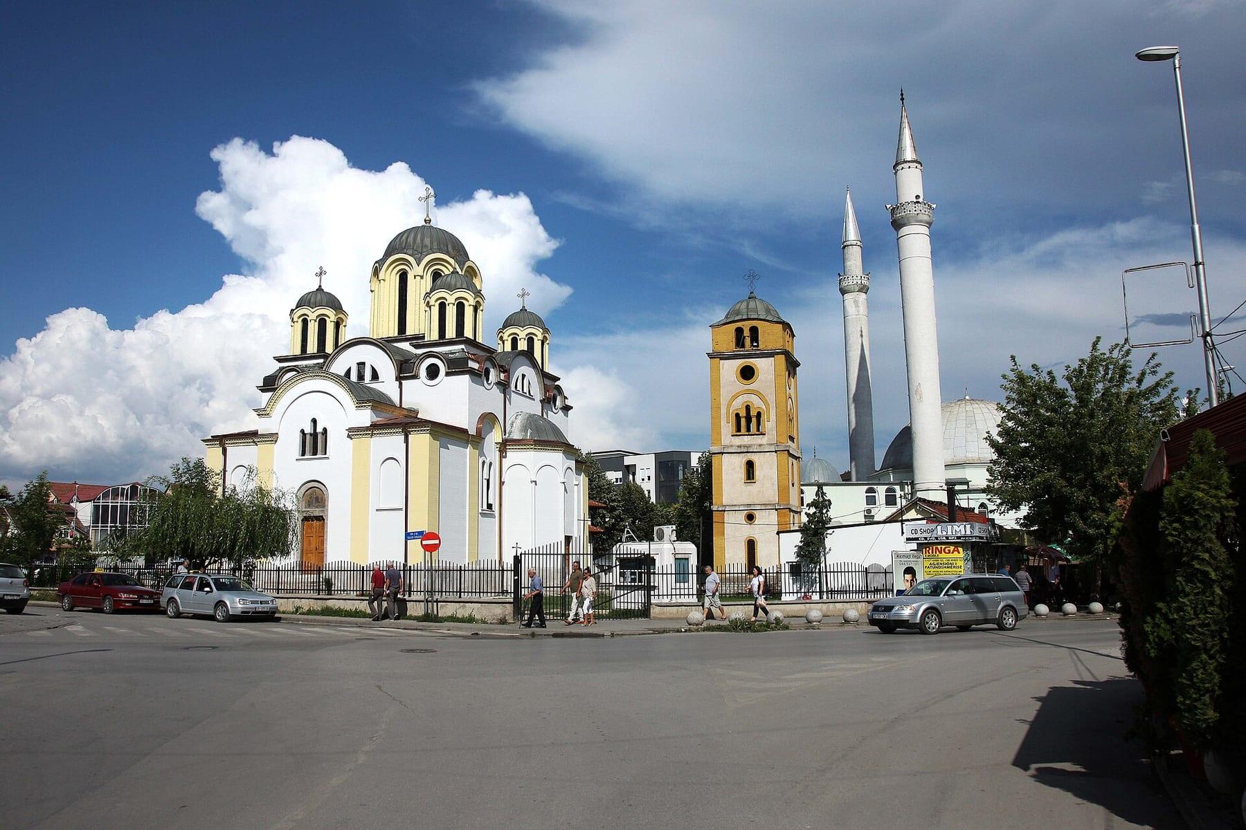 Domed Orthodox church next to a mosque with two minarets under a cloudy sky.